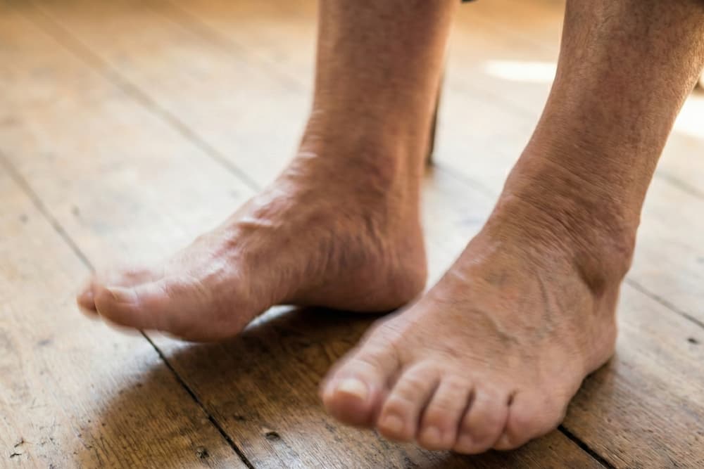 Et nærbillede af to bare fødder midt i luften, der ser ud til at hoppe eller danse over en glat, lys overflade med en grå baggrund. Bevægelsessløring fremhæver føddernes bevægelse.