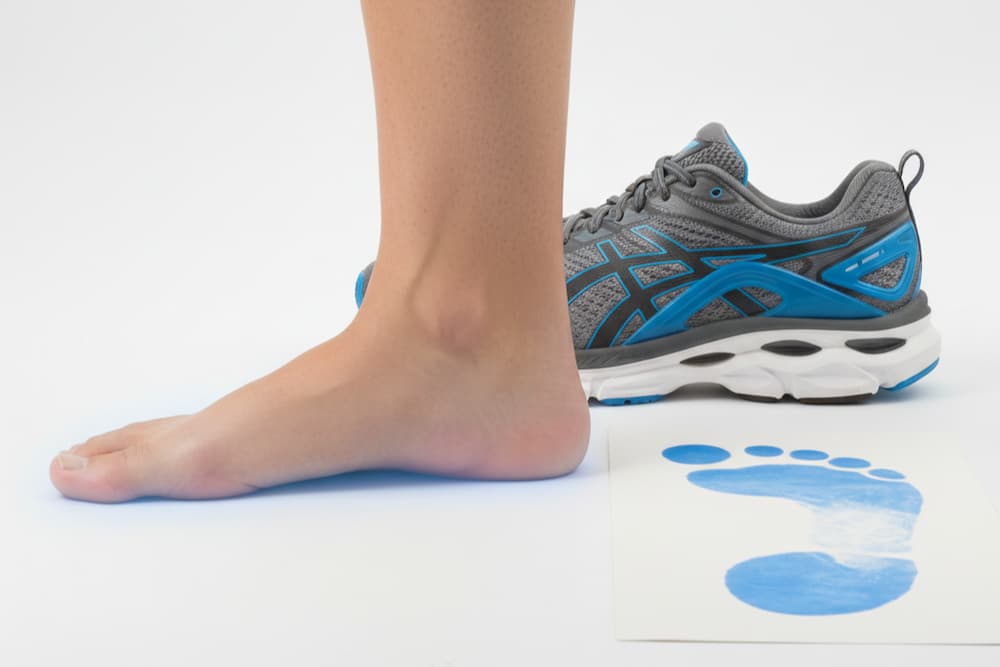 En barfodet menneskefod ved siden af en mørkeblå sportssko med hvid sål på en mørk baggrund, der fremhæver en sammenligning mellem bare fødder og fodtøj.