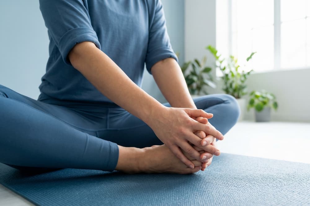 Nærbillede af to bare fødder på en flad overflade, hvor hænderne forsigtigt holder tæerne. Neglene på både hænder og fødder er pænt klippede og rene. Belysningen kaster bløde skygger.