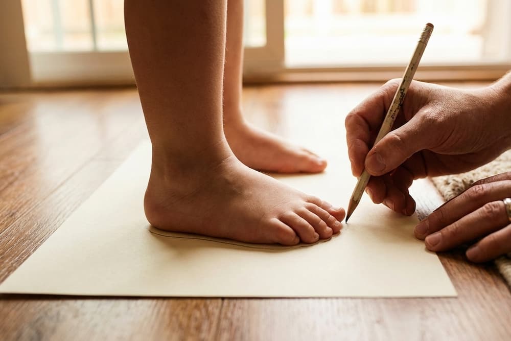 En person iført en brun sweater tegner en simpel skitse af et ansigt på et hvidt ark papir med en blyant, mens han sidder ved et træbord.